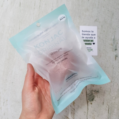 Esponja Konjac facial con arcilla roja en su empaque original, sostenida por una mano.
