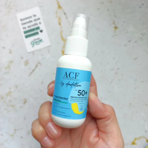 Botella de fotoprotector Toque Seco de Dadatina, con FPS 50+, en una mano sobre fondo claro.