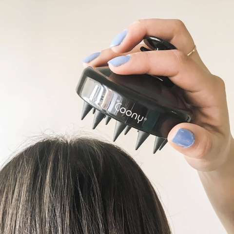 Masajeador de cuero cabelludo negro de la marca Coony en uso, sostenido por una mano sobre el cabello.