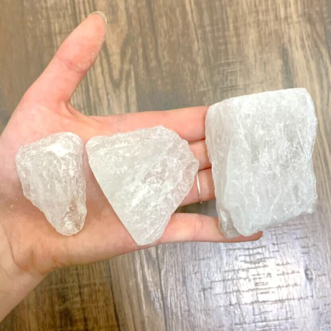 Tres piezas de piedra de alumbre en la palma de una mano, mostrando diferentes tamaños y formas.