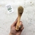 Una mano sostiene un cepillo de limpieza facial de madera con cerdas suaves, junto a una tarjeta de Tiendas Green que promueve el cuidado del planeta.