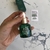 Frasco de aceite facial antioxidante reparador de la marca BEK, con tapa y gotero, sostenido por una mano. Fondo con diseño abstracto.