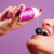 Uma mulher segurando um frasco de gel excitante Vibration Power Amora, vertendo o produto sobre uma amora enquanto sorri.
