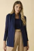 Colete de alfaiataria azul marinho feminino, usado sobre blusa de manga longa azul e calça bege, em fundo neutro.