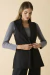 Colete de alfaiataria preto feminino, sem mangas, com lapela, usado sobre blusa de manga longa cinza.