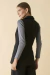Modelo vestindo um colete de alfaiataria preto, visto de costas, com uma blusa de mangas compridas cinza por baixo.