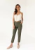 Modelo vestindo calça Amanda verde militar, combinada com blusa branca de alças finas e cinto bege, em ambiente claro.