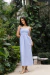 Modelo vestindo o Vestido Tricoline Mila Azul, longo e de alças finas, posando em um jardim com vegetação ao fundo.