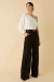 Modelo vestindo Tricot Milena Off White, blusa de um ombro só, combinada com calça preta e acessórios elegantes.