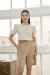 Modelo vestindo a Blusa Giulia Marfim de manga curta, combinada com bermuda bege, em ambiente iluminado por janelas grandes.