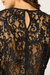 Detalhe das costas de uma blusa de renda preta feminina, com fechamento por botão e padrão floral vazado.