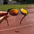Óculos de sol esportivo HSTN na cor Ruby, com lente espelhada em tons de laranja e vermelho, acompanhado de uma case de proteção.