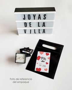 Aretes tipo topo en forma de mariposas, presentados en una caja negra. Incluye una bolsa de empaque con un mensaje de "Feliz día".