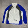 Jaqueta corta vento Oakley nas cores azul, branco e cinza, com zíper na parte frontal.