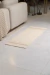 Passadeira Boho Delicate Caramelo em um ambiente de sala, posicionada sobre piso claro ao lado de um sofá bege.