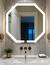 Espejo LED ARD Glanz OctaGlow en forma octagonal, instalado en un baño moderno con mármol y grifería dorada.