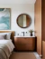 Round wooden mirror displayed above a bedside table in a modern bedroom setting.