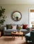 Round wooden mirror in a living room setting, above a light blue sofa with decorative pillows and a coffee table.
