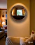 A round wooden mirror with a dark oak frame, mounted on a warm-toned wall, reflecting a cozy living room.