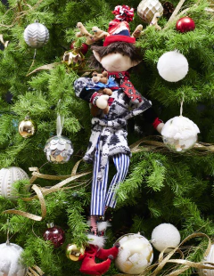 Muñeco de duende decorativo con bata blanca y gris, portando un peluche de osito en brazos, vestido con un gorro de Navidad y pantalones de rayas.