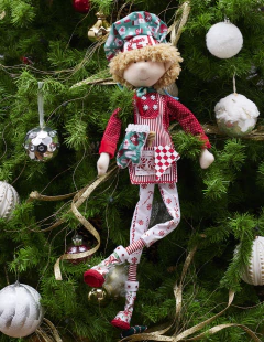 Peluche del Duende Chef "Sugar" de 70 cm, vestido con un delantal rojo y decoraciones navideñas, colgado de un árbol de Navidad.