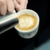 Taza de té porcelana decorada con un diseño colorido, siendo llenada con café con arte latte en la superficie.
