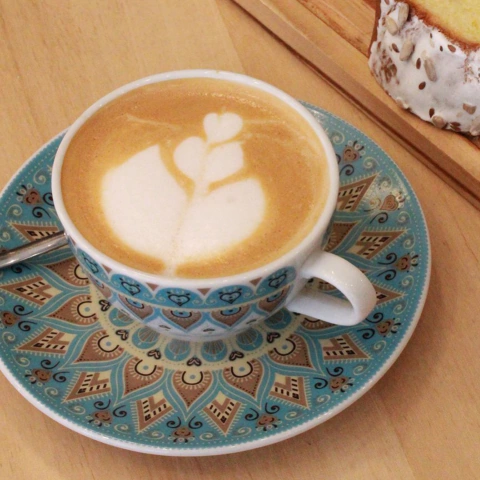 Taza té porcelana con un diseño colorido y un latte art en forma de hoja, acompañada de un plato