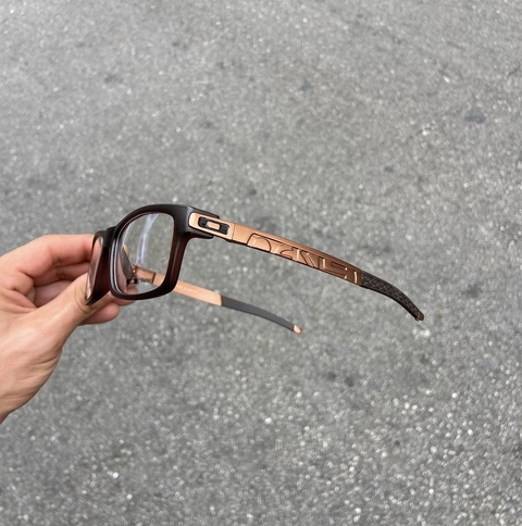 Armação de óculos OKL Copper P com design moderno, em tons de preto e cobre, sendo segurada por uma mão.