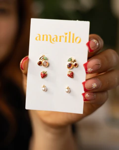 Set de tres pares de aretes dorados con diseño de cerezas, fresas y perlas en tarjeta blanca con logo amarillo