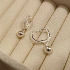 Brinco argolinha cravejada com pingente de bolinha em prata 925, exibido em um suporte de joias.