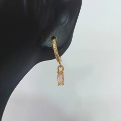 Brinco argolinha dourado cravejado com zircônias e pingente com pedra navete rosa, usado em orelha de manequim preto