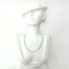 Conjunto de semijoias femininas com colar de cristais azul claro e brinco dourado com cristais azul claro em busto branco