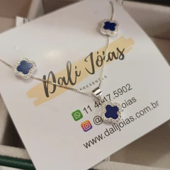Conjunto de joias em prata 925 com zircônias cristal e detalhe em azul, incluindo colar e brincos no formato de trevo.