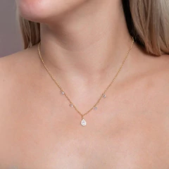Colar gota cravejado de zircônias em corrente dourada, adornado com pequenas pedras, em destaque no pescoço de uma modelo.