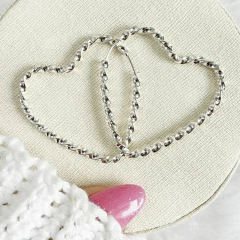 Brinco argola em forma de coração, torcido, feito em prata 925, sobre uma superfície clara.