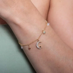 Pulseira cravejada de zircônias com pendentes de lua e estrelas, em um braço feminino.