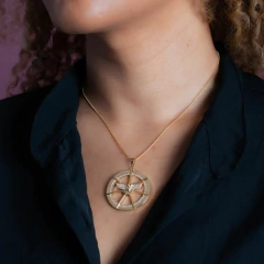 Colar Espírito Santo cravejado de zircônias, pendurado no pescoço de uma mulher com cabelo cacheado e blusa preta.