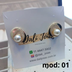 Brincos folheados com pérola, design elegante, apresentados em um cartão de marca.