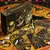 Conjunto esotérico Tarô Gold Deluxe com cartas de tarô e caixa decorativa sobre um pano astrológico.