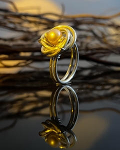 Anel Saturno Rose com design elegante e uma pérola amarela no centro, refletindo em uma superfície escura.