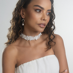Modelo usando um choker de conchas brancas, com cabelo solto e brincos elegantes.