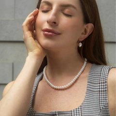 Modelo usando um colar de pérolas bivalves, com expressão serena e sorriso suave.