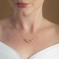 Colar delicado com quatro pérolas em tons de branco e cinza, usado no pescoço de uma mulher com blusa branca