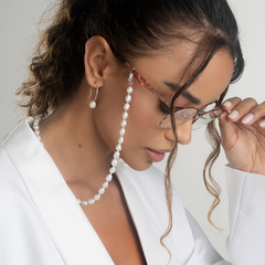 Mulher usando óculos com cordão de pérolas, destacando estilo e elegância.