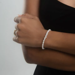 Pulseira de pérolas branca em um braço feminino.