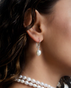 Brinco Paros com design elegante, apresentando uma pérola pendurada, usado por uma modelo com cabelo solto.