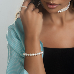 Pulseira Lua M em pérola, adornando o pulso de uma modelo, com blusa azul listrada ao fundo.