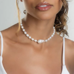 Modelo usando um colar barroco de pérolas brancas, com um olhar suave e elegante.