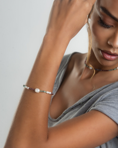 Pulseira Riviera colorida com pérolas, adornando o pulso de uma mulher, destacando seu estilo e elegância.