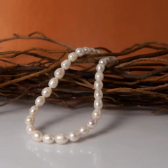 Colar Luminare com pérolas naturais dispostas sobre galhos secos em fundo laranja